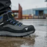 Zapatilla de seguridad impermeable Aquaman pisando un charco sobre concreto húmedo en un patio industrial